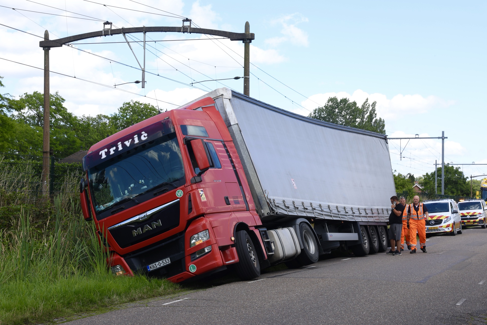 Vrachtwagen in sloot naast spoor, treinen rijden stapvoets