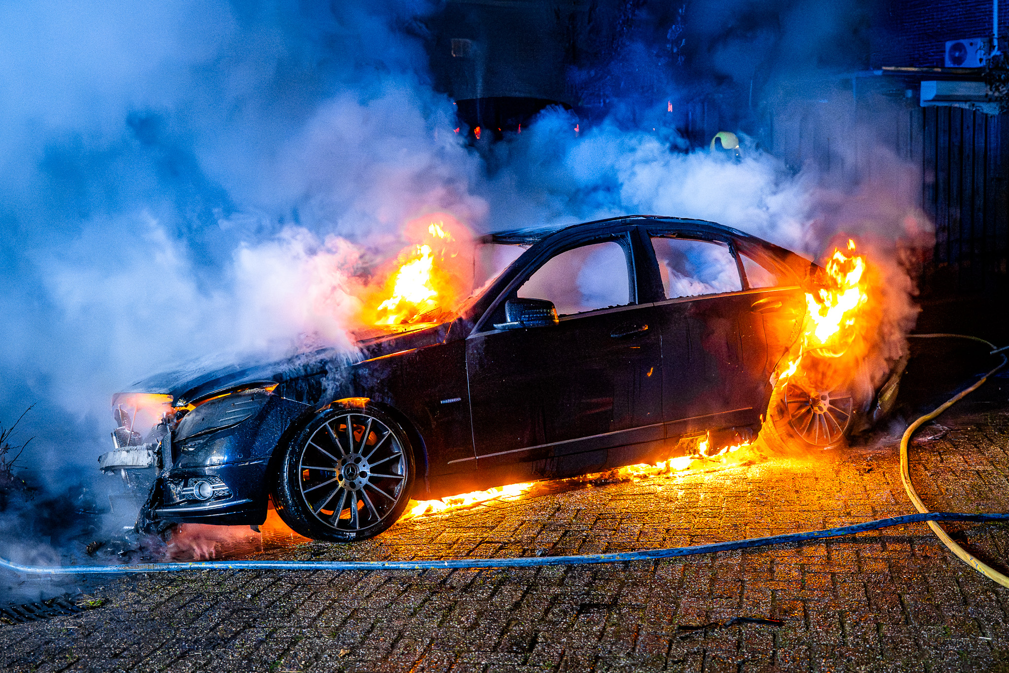 Auto verwoest door brand, vlammen slaan over naar schutting