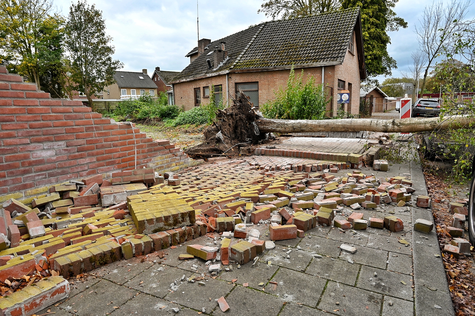 Boom waait om door harde wind, muur stort deels in