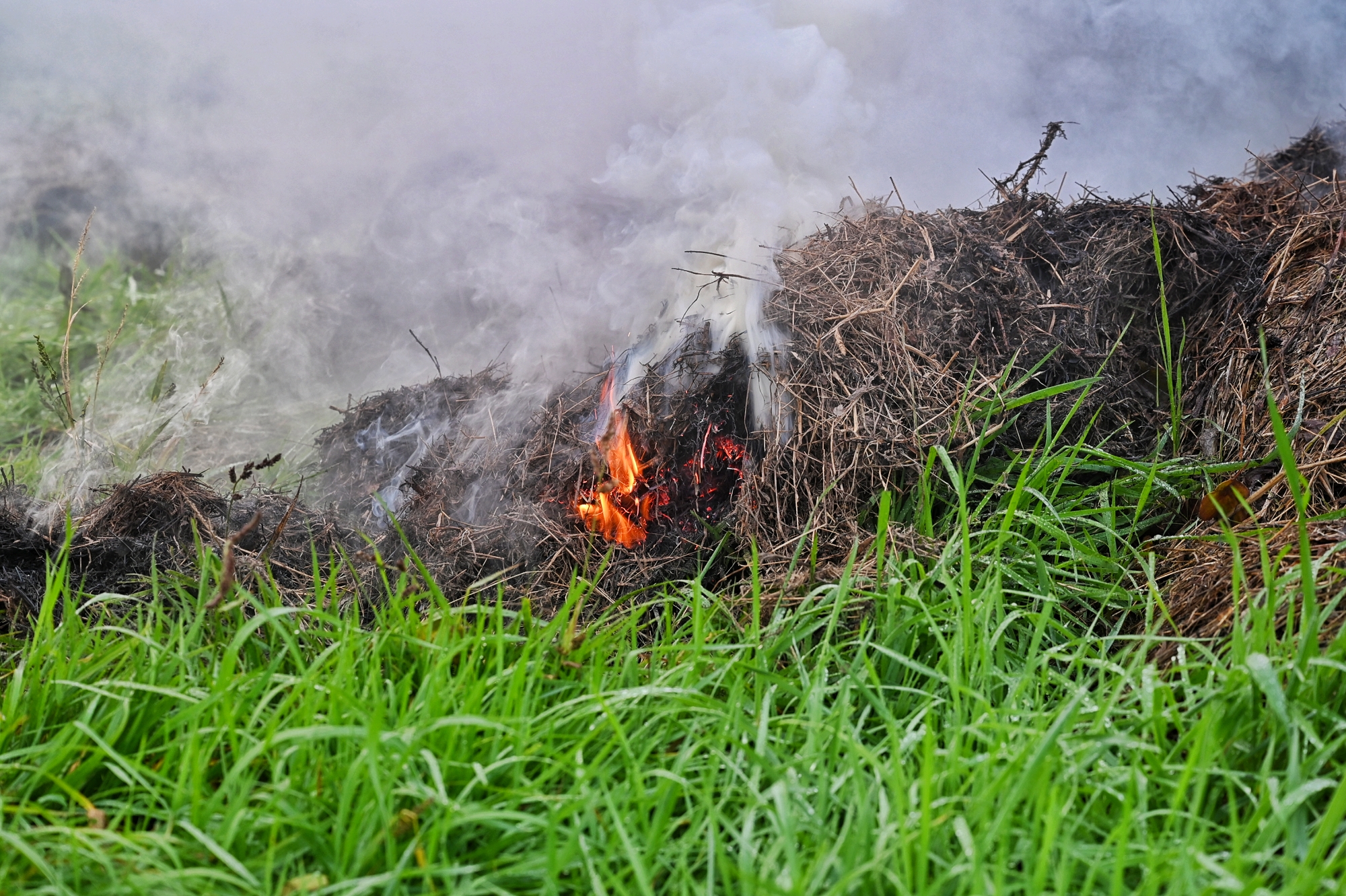 Brandweer blust smeulende berg maai-afval