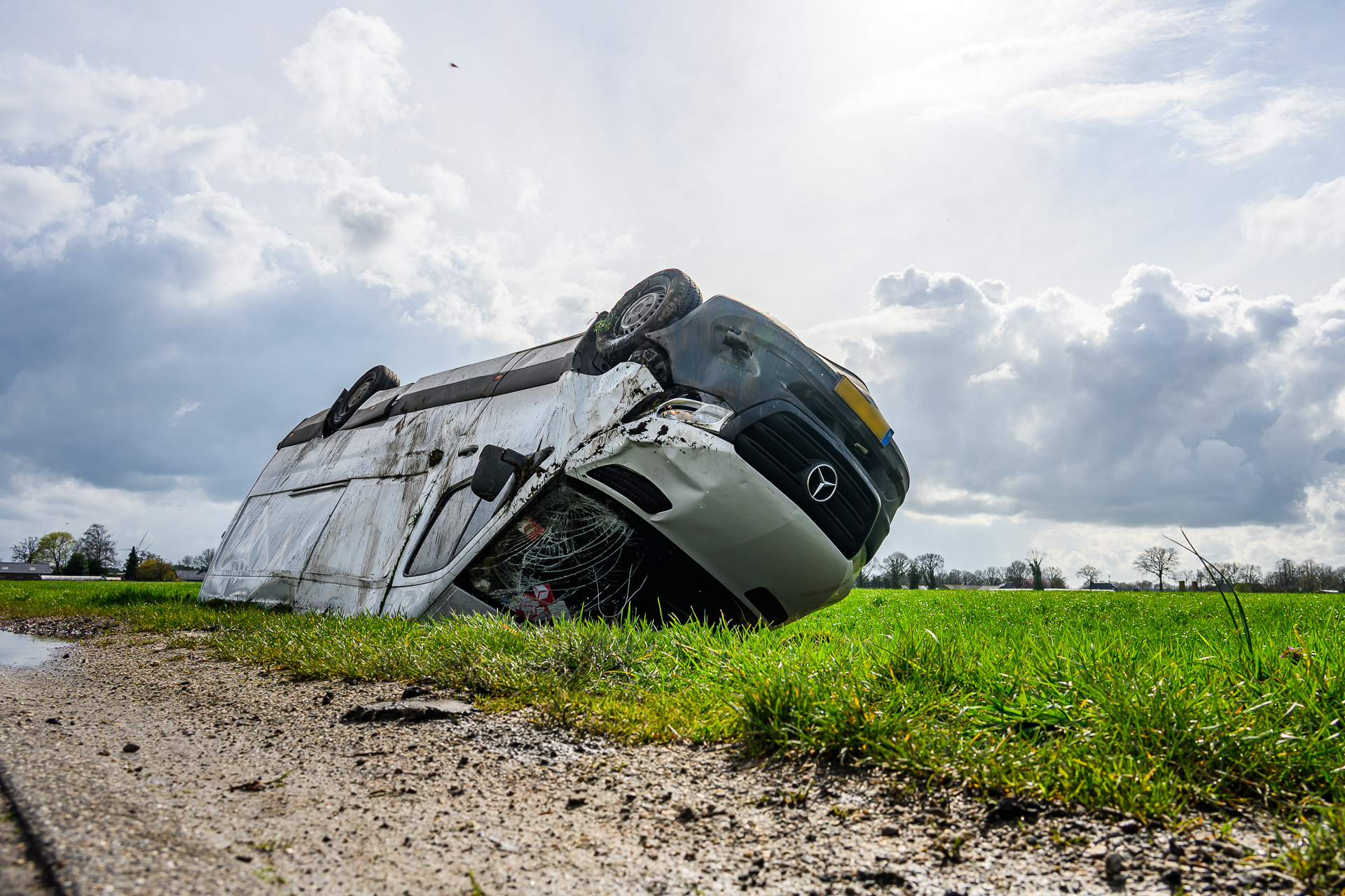 Bestelbus van pakketbezorger op zijn kop in sloot