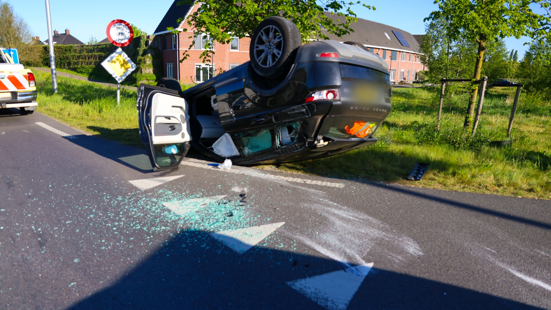 Overturned dark SUV on a road with broken glass scattered on the asphalt and a police vehicle nearby; back and side doors open, incident appears recent in a residential area.