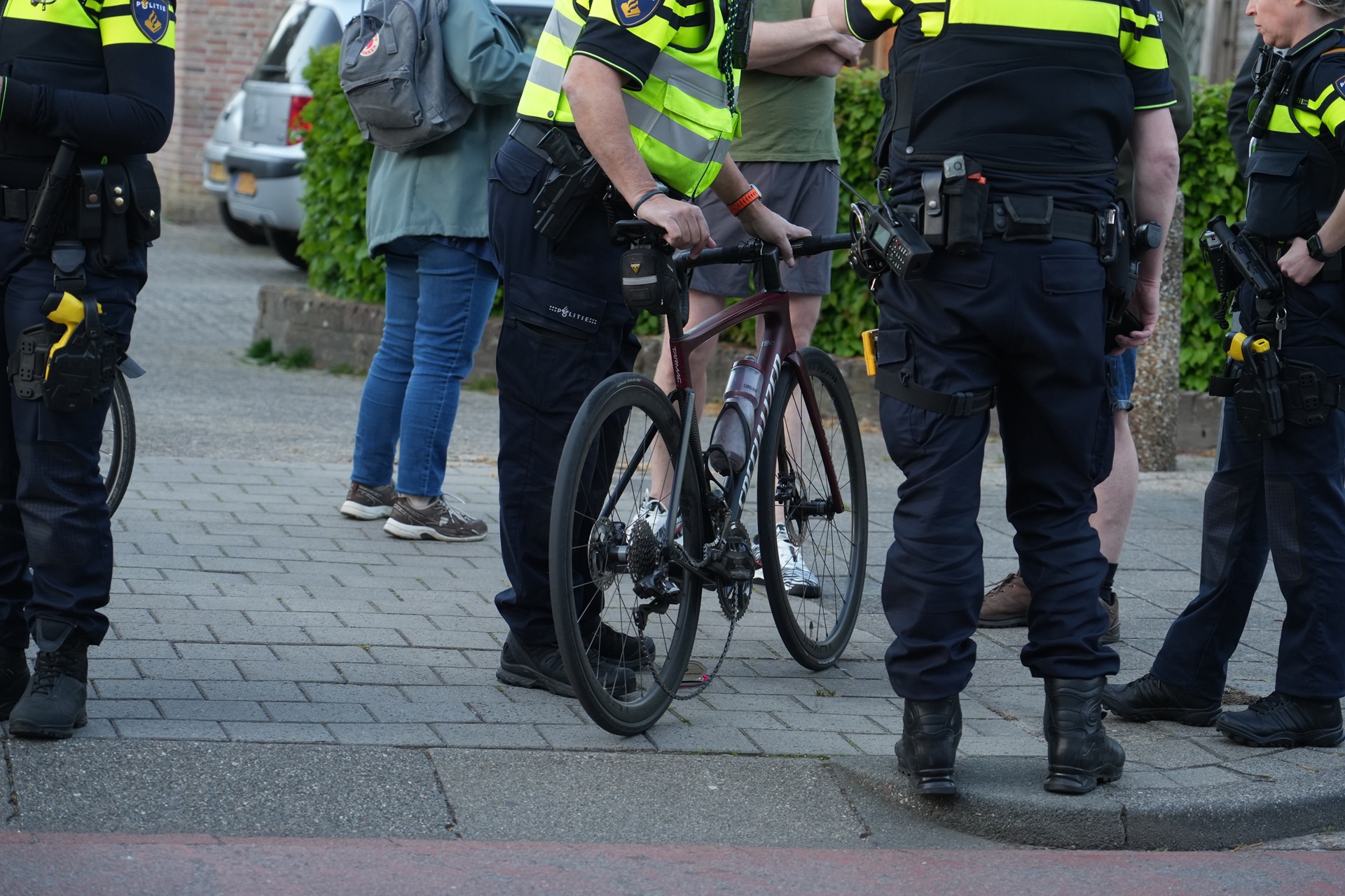 Group of police officers in high-visibility vests standing around a brown road bike on a sidewalk.